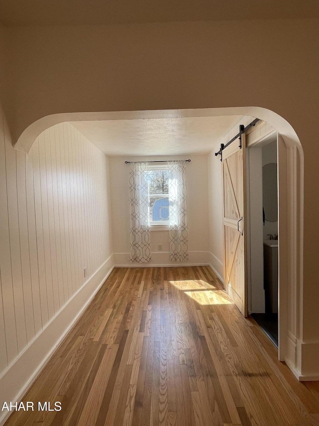 empty room with a barn door, arched walkways, baseboards, and hardwood / wood-style flooring