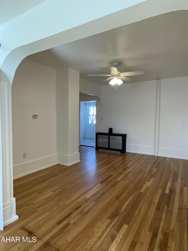 spare room with baseboards, wood finished floors, arched walkways, and ceiling fan