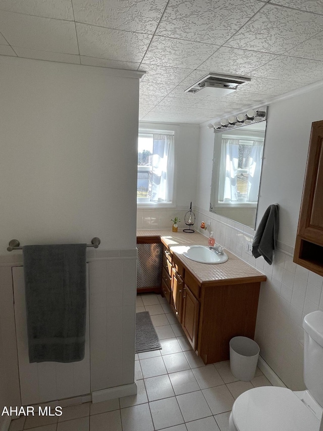 bathroom with vanity, a wainscoted wall, visible vents, tile walls, and toilet