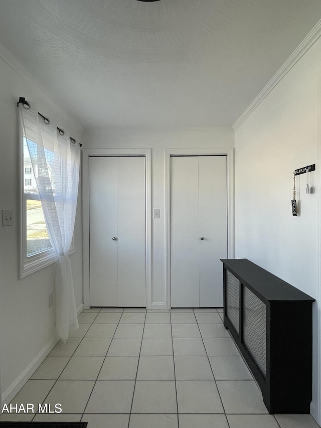 unfurnished bedroom with light tile patterned floors, baseboards, multiple closets, and ornamental molding