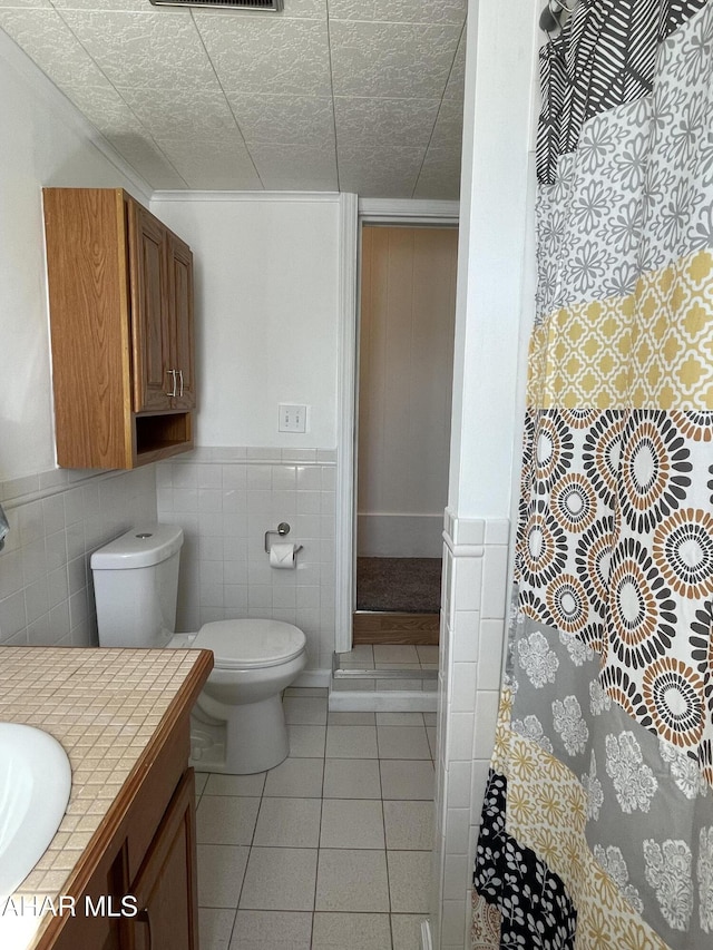 bathroom with toilet, vanity, wainscoting, tile patterned floors, and tile walls