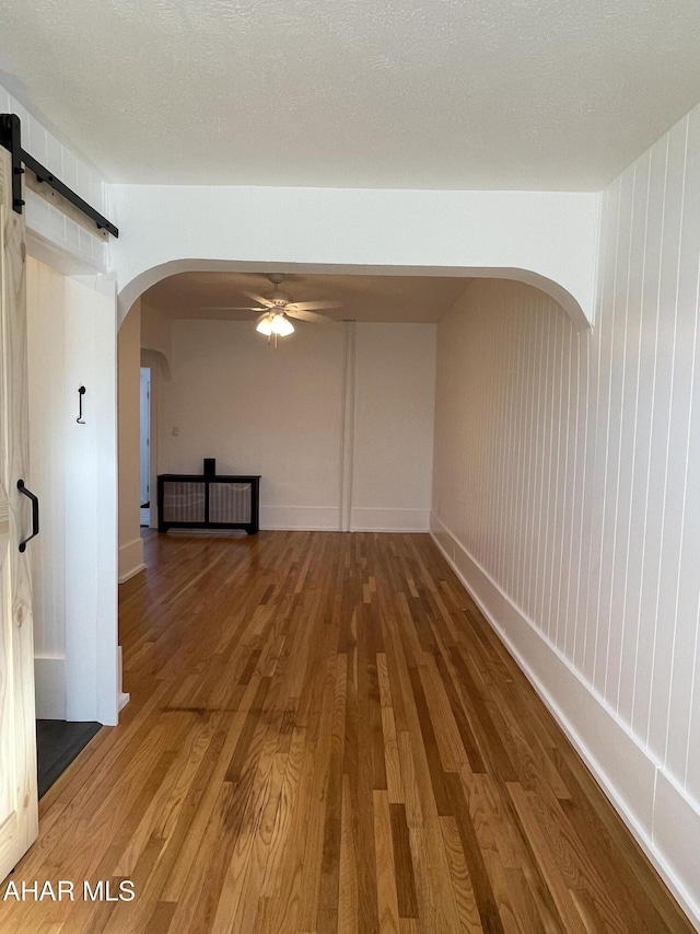 spare room featuring a barn door, a textured ceiling, wood finished floors, and a ceiling fan