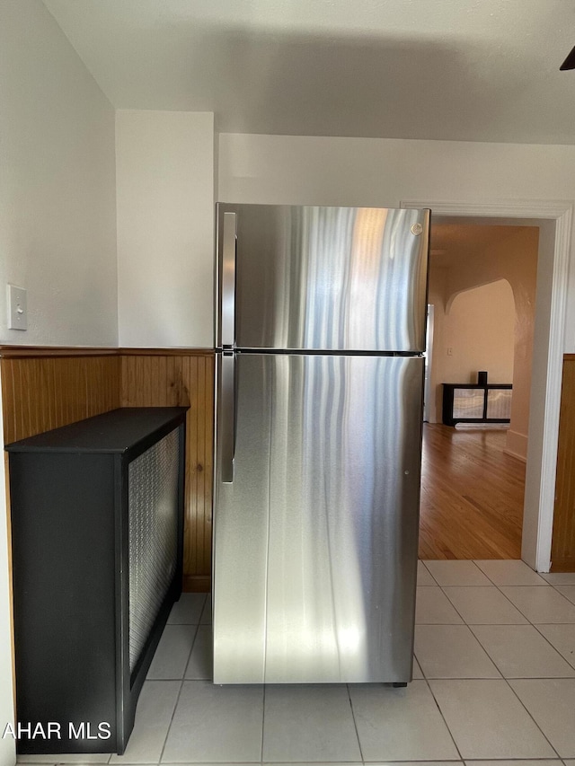 kitchen featuring wooden walls, light tile patterned flooring, wainscoting, and freestanding refrigerator