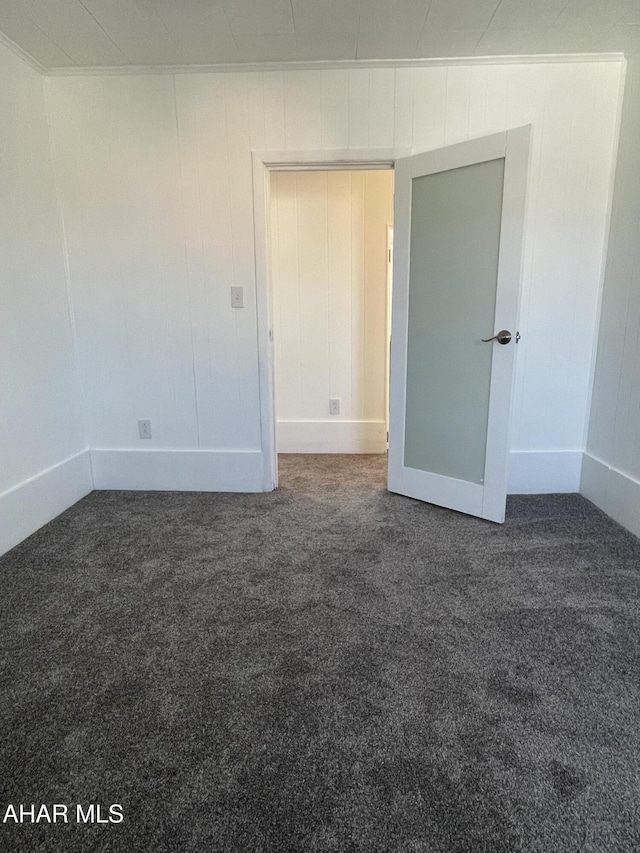 spare room featuring ornamental molding and dark carpet