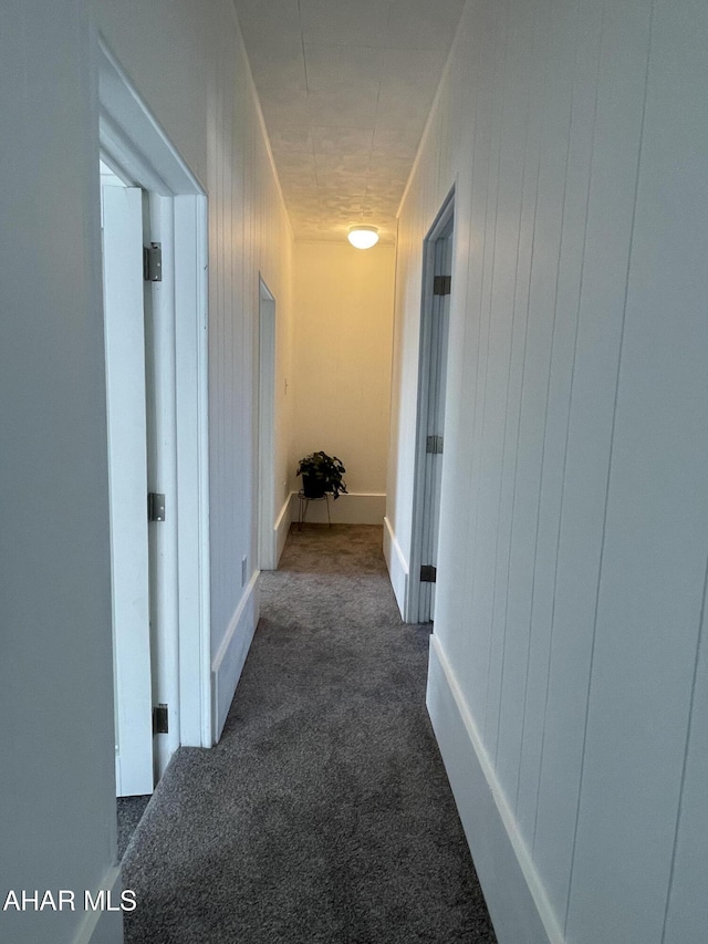 hall featuring wooden walls and dark colored carpet