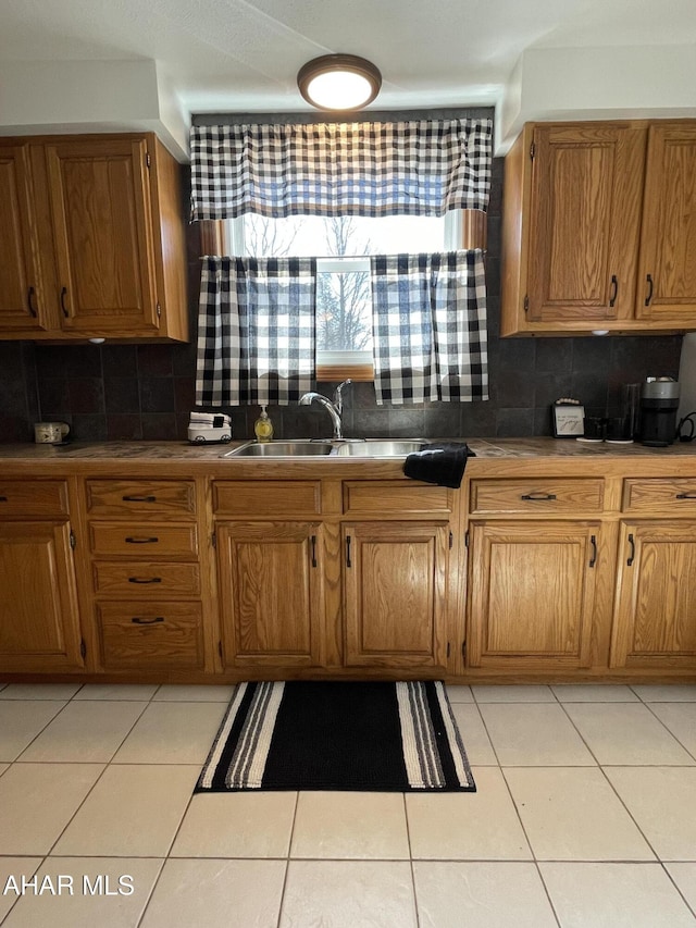 kitchen with light tile patterned floors, backsplash, brown cabinetry, and a sink