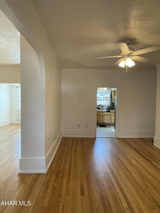 unfurnished room featuring light wood finished floors, baseboards, ceiling fan, arched walkways, and a textured ceiling