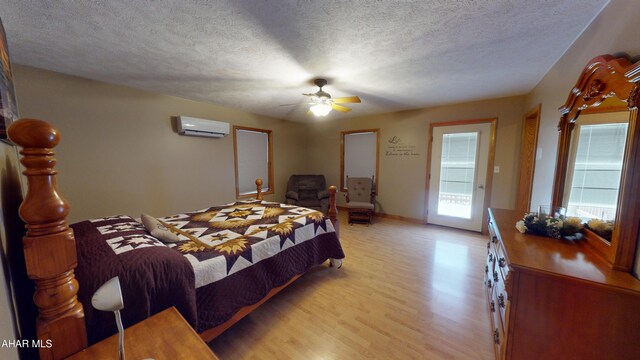 bedroom featuring access to exterior, a textured ceiling, a wall mounted AC, ceiling fan, and light hardwood / wood-style flooring