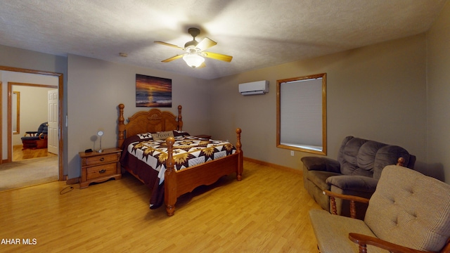 bedroom with ceiling fan, light hardwood / wood-style floors, a textured ceiling, and a wall mounted AC