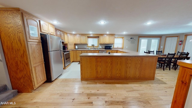 kitchen with light wood-type flooring, kitchen peninsula, sink, and appliances with stainless steel finishes