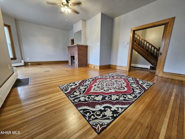 living room with a fireplace, wood-type flooring, baseboard heating, and ceiling fan