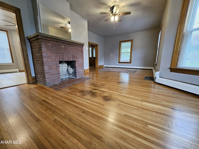 unfurnished living room with a fireplace, light hardwood / wood-style floors, ceiling fan, and a baseboard heating unit