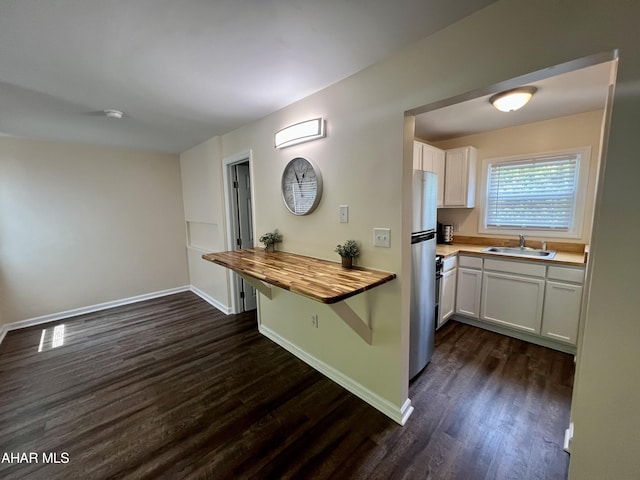 kitchen with sink, butcher block counters, dark hardwood / wood-style floors, white cabinetry, and stainless steel refrigerator