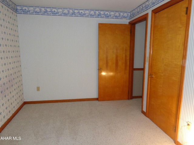 carpeted spare room featuring wallpapered walls and baseboards