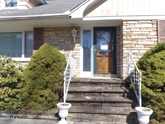 doorway to property featuring board and batten siding, stone siding, and a shingled roof