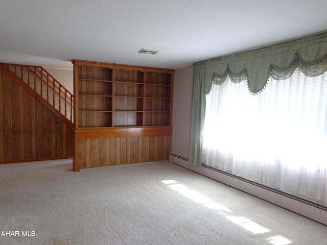 unfurnished living room featuring stairway, carpet, visible vents, wood walls, and baseboard heating