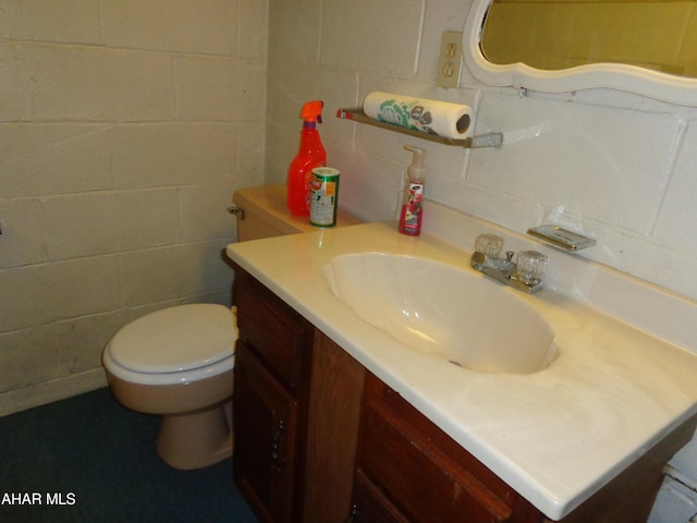 half bathroom with toilet, vanity, and concrete block wall