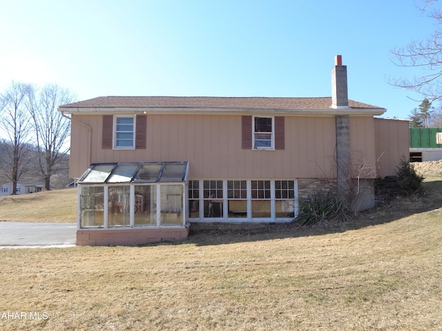 rear view of property with a lawn, roof with shingles, and a chimney