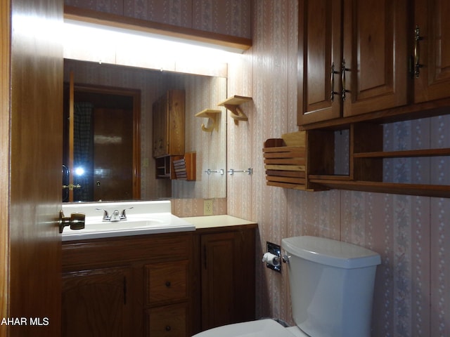 bathroom featuring vanity, toilet, and wallpapered walls