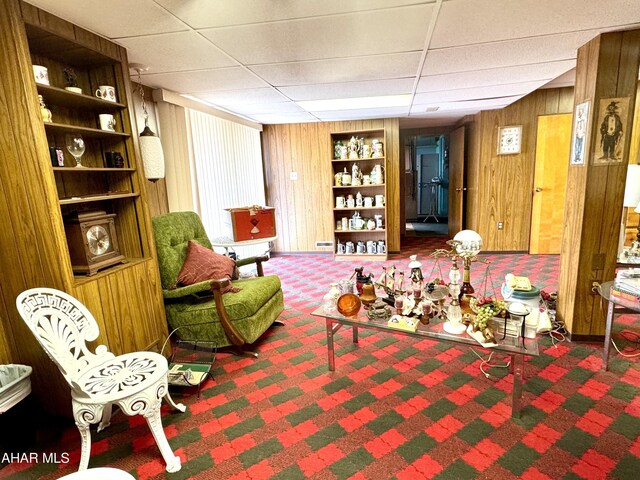 living area with carpet flooring, wood walls, and a paneled ceiling