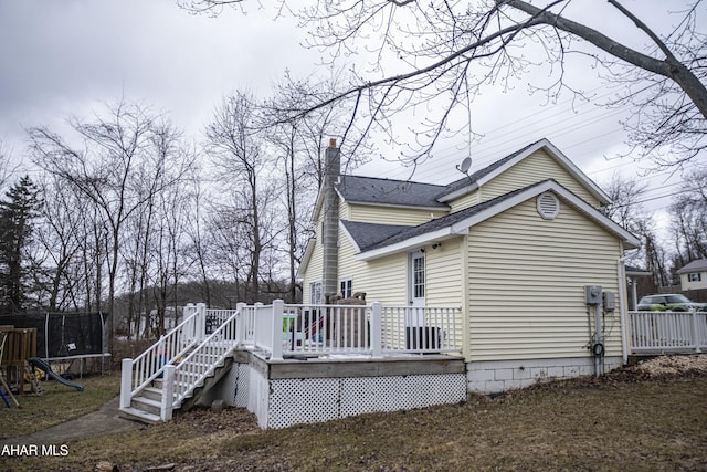 exterior space with a deck, a chimney, a trampoline, and a shingled roof