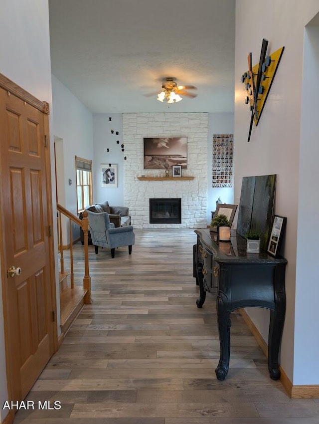 living area featuring a fireplace, a ceiling fan, and wood finished floors