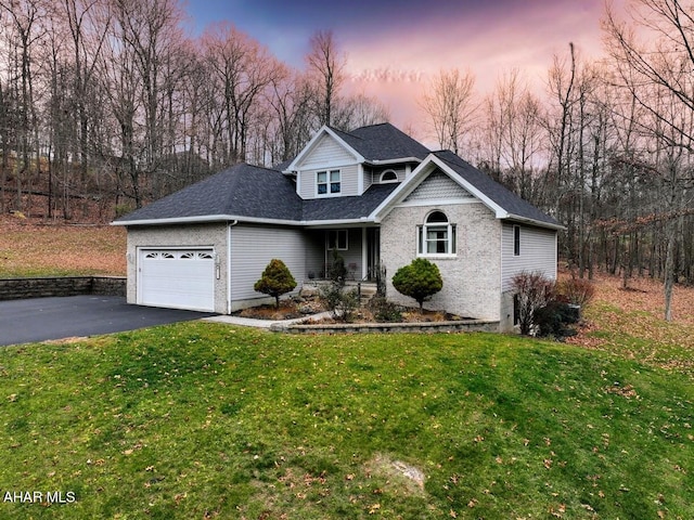 traditional-style home featuring aphalt driveway, a yard, roof with shingles, an attached garage, and brick siding