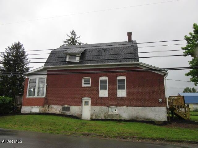 view of property exterior featuring brick siding, stairway, roof with shingles, and a yard