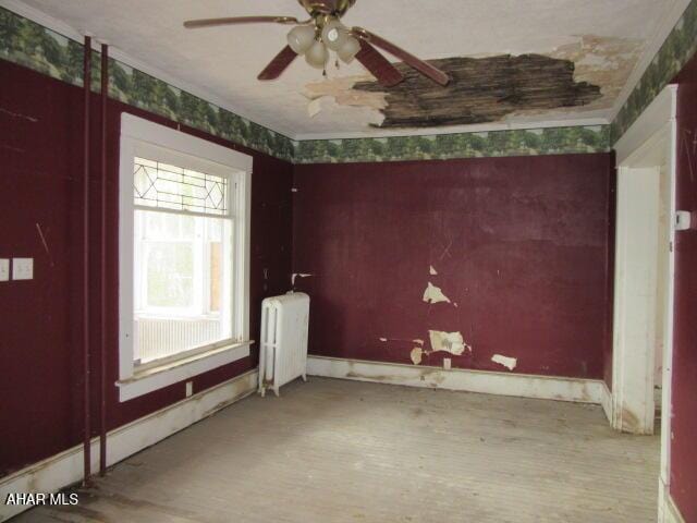 empty room with radiator, a ceiling fan, wood finished floors, and baseboards