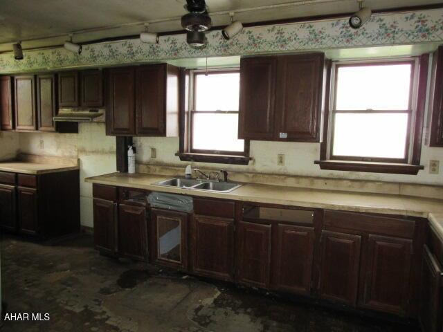 kitchen with a sink, light countertops, wallpapered walls, and dark brown cabinets