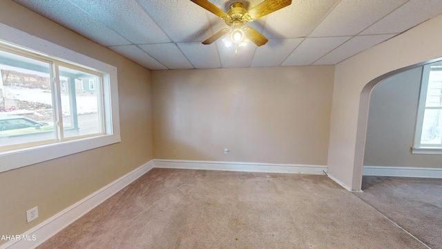 empty room with ceiling fan, a drop ceiling, and light carpet