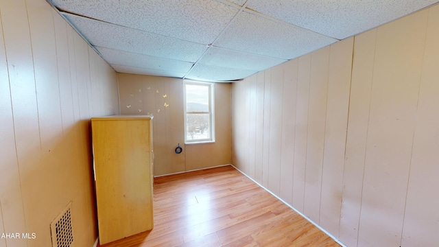 spare room featuring wood-type flooring, a drop ceiling, and wood walls