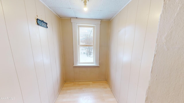 hall with a paneled ceiling, a wealth of natural light, and wood walls