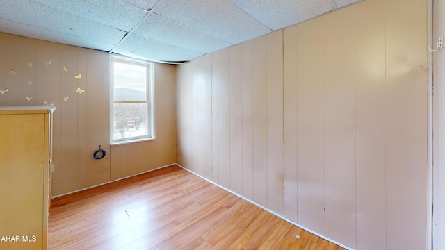 unfurnished room with wood walls, a paneled ceiling, and hardwood / wood-style flooring