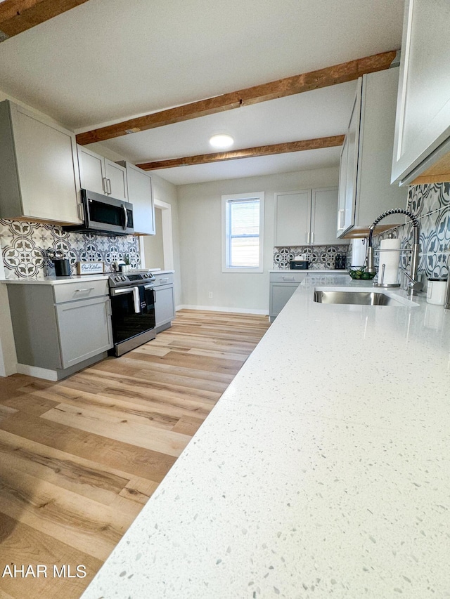 kitchen with appliances with stainless steel finishes, tasteful backsplash, sink, light hardwood / wood-style floors, and beam ceiling