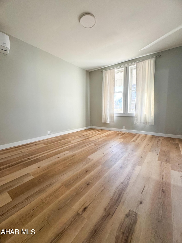 empty room with a wall unit AC and light wood-type flooring