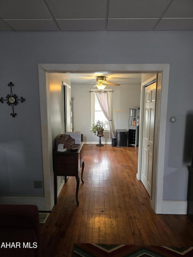 hall with a paneled ceiling, baseboards, and hardwood / wood-style floors