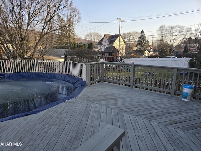 wooden terrace with a playground and a fenced backyard