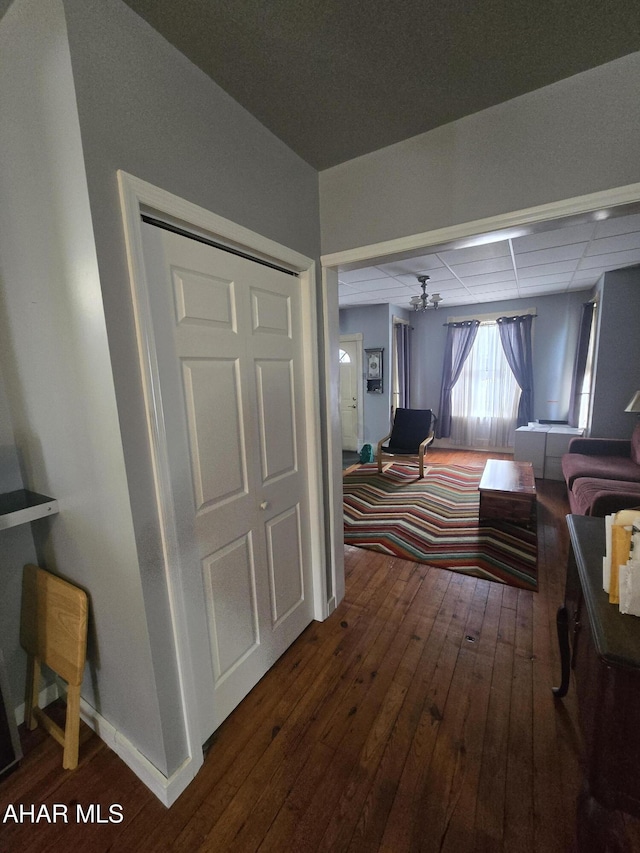 hallway with a paneled ceiling, baseboards, and wood-type flooring