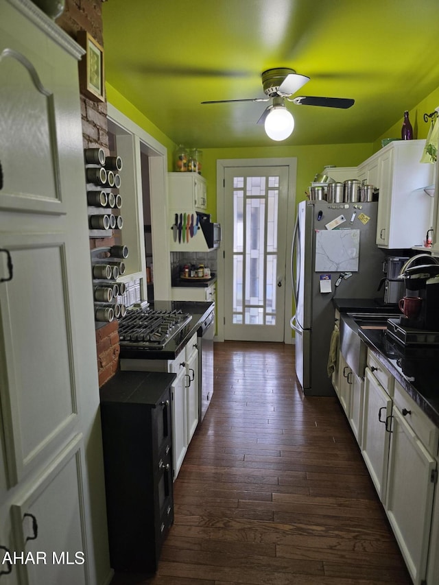 kitchen with dark countertops, dark wood finished floors, appliances with stainless steel finishes, white cabinets, and ceiling fan