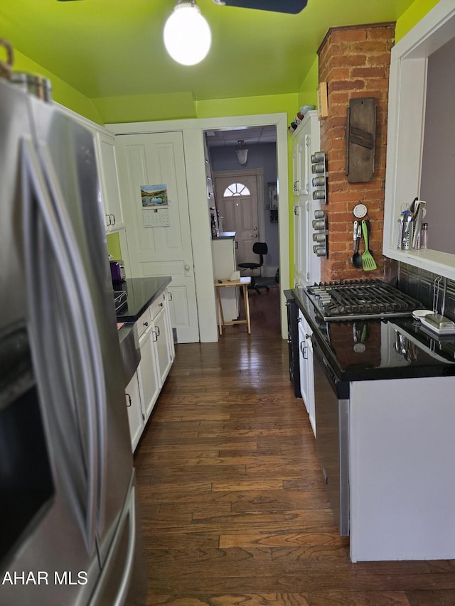 kitchen with dark countertops, backsplash, dark wood finished floors, stainless steel fridge, and white cabinetry