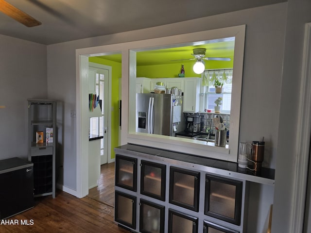 kitchen featuring dark wood-type flooring, white cabinets, stainless steel fridge with ice dispenser, baseboards, and ceiling fan