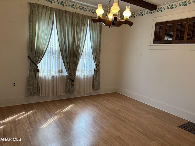 empty room featuring a chandelier, wood-type flooring, and beam ceiling