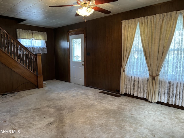 carpeted foyer entrance with ceiling fan and wood walls