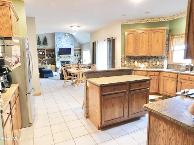 kitchen featuring a center island, sink, a stone fireplace, vaulted ceiling, and light tile patterned floors