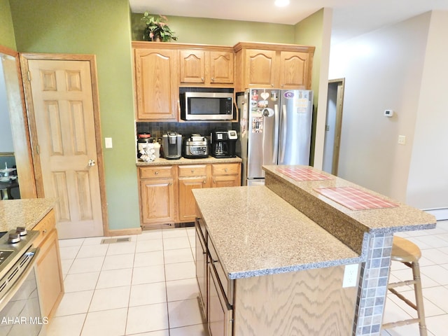 kitchen with stainless steel appliances, light tile patterned floors, light stone counters, a kitchen bar, and a kitchen island