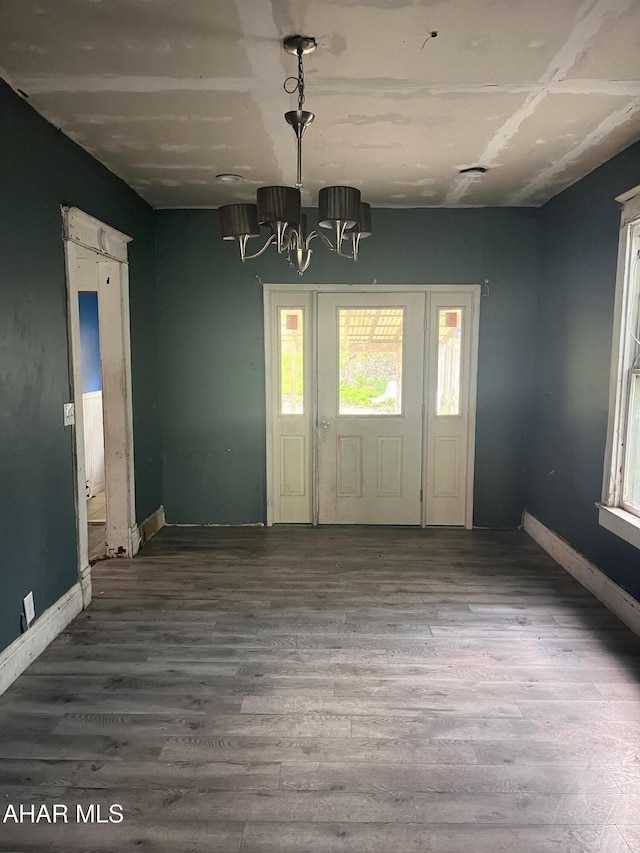 unfurnished dining area featuring baseboards, an inviting chandelier, and wood finished floors