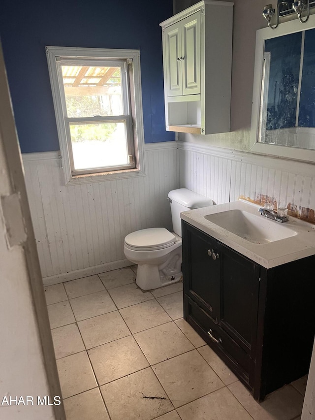 half bathroom with tile patterned floors, toilet, wainscoting, and vanity