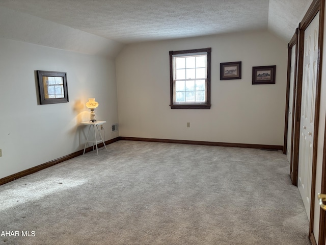 unfurnished bedroom featuring light carpet, a textured ceiling, and lofted ceiling