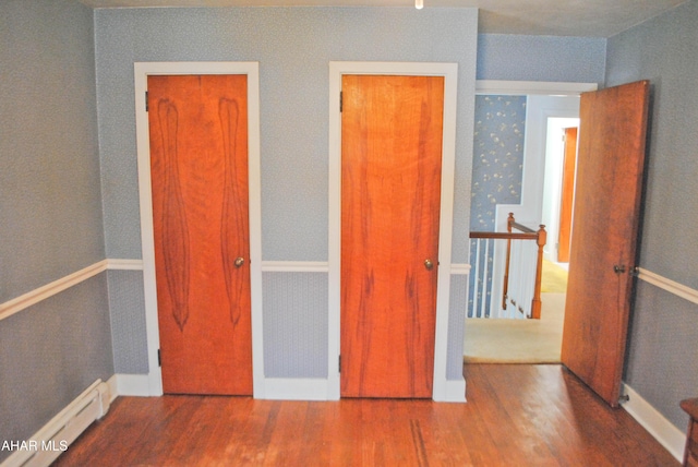 unfurnished bedroom with a baseboard radiator, baseboards, and wood finished floors